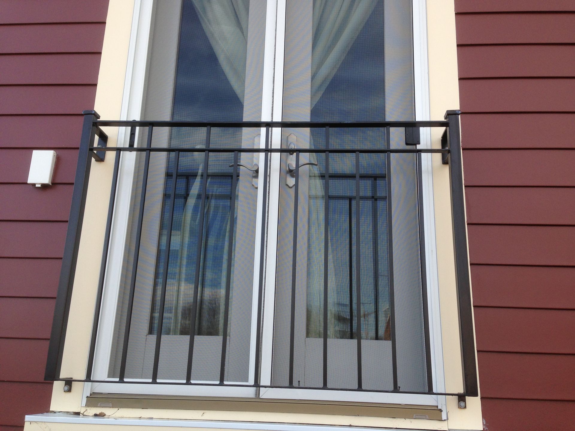 White-framed window with a black railing on a red building exterior.