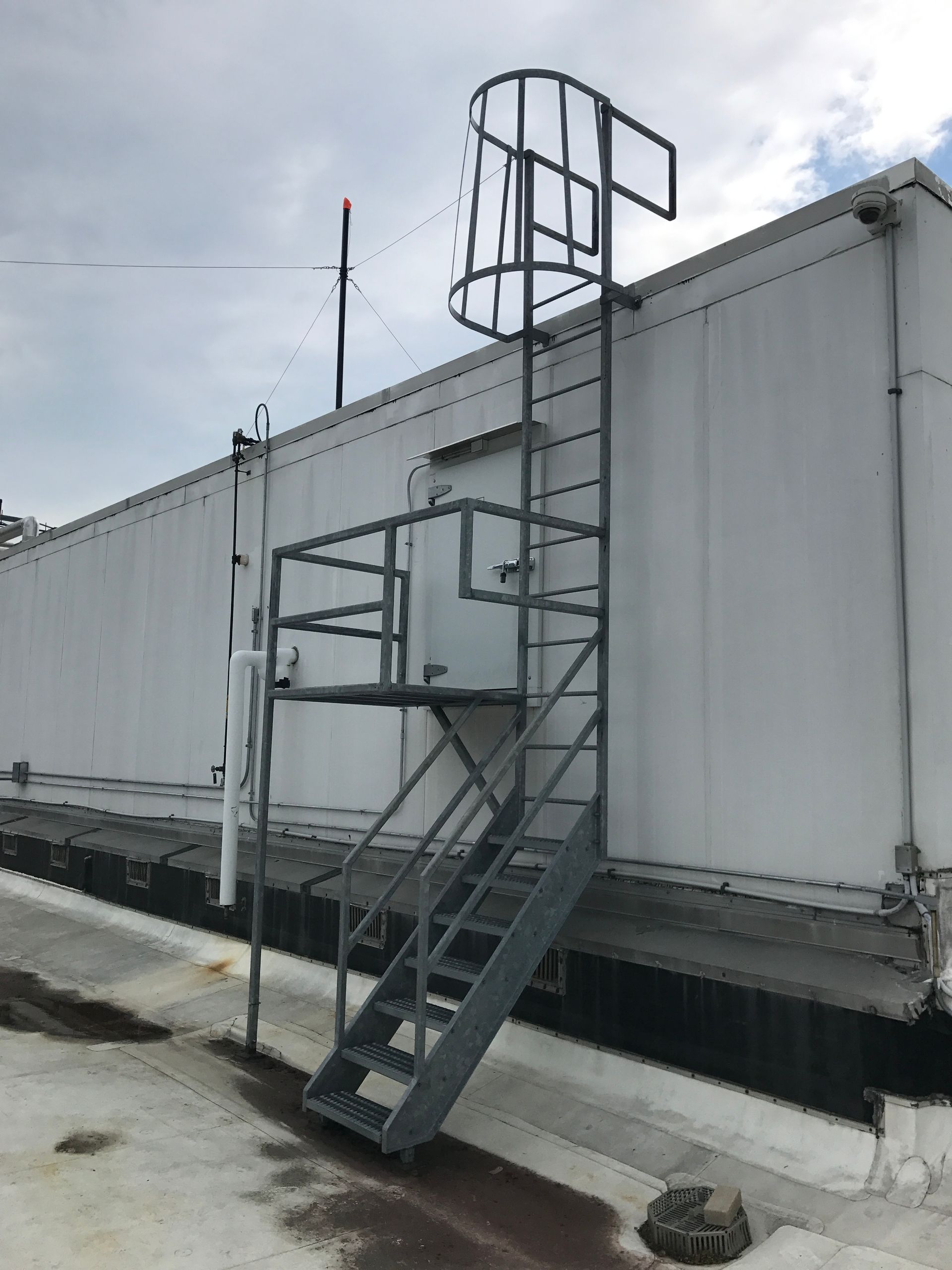 Metal staircase and landing attached to a white industrial trailer under a cloudy sky.