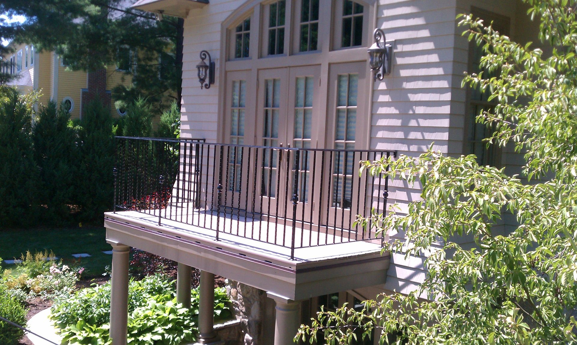 Small white porch with black railing on a house, surrounded by green shrubs and trees