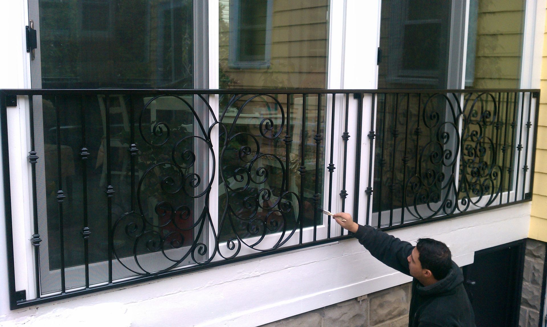 Man pointing up at ornate black balcony railing outside a building
