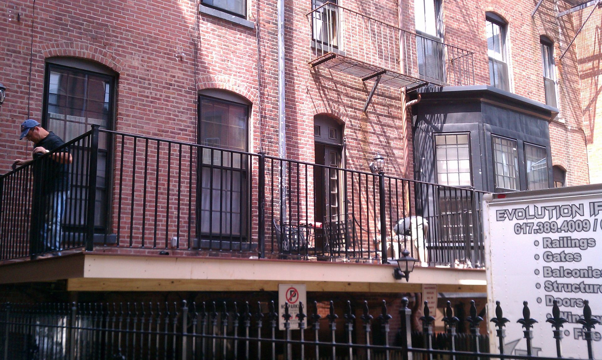Brick apartment building with black balconies and a person on the left, beside a signboard and awning