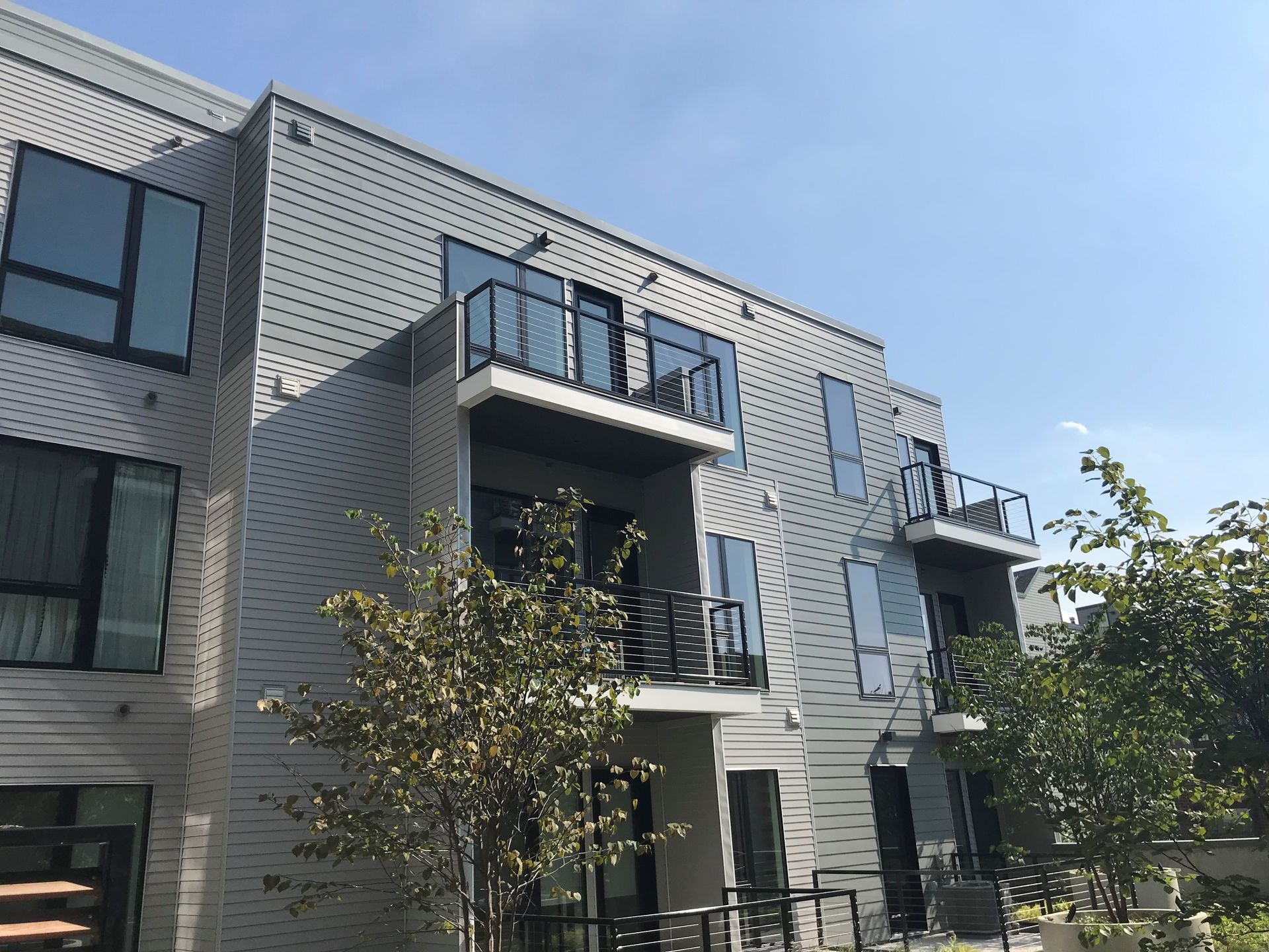 Modern apartment building with gray brick facade, black balconies, and trees in front