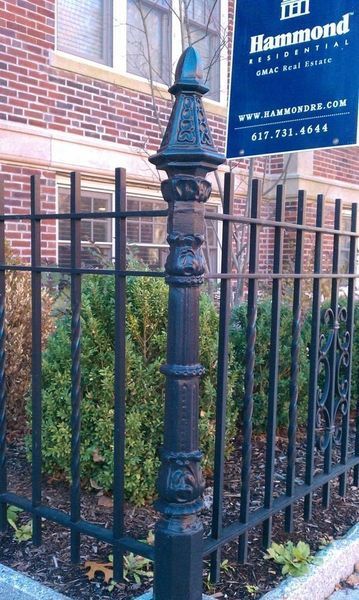 Decorative black metal fence post and iron railing in front of a brick building with a Hammond Real Estate sign.