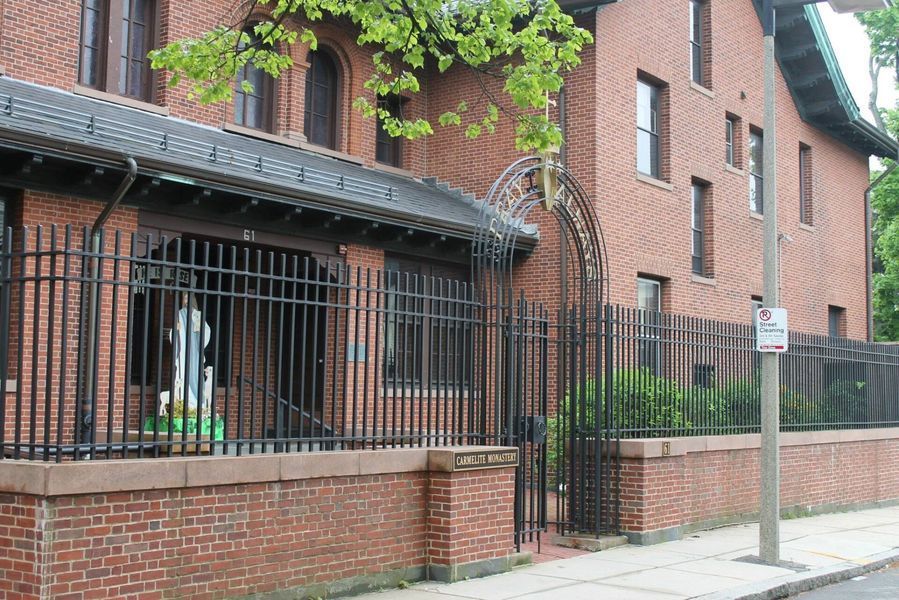 Red brick building with a black iron fence and arched gate, surrounded by trees on a city street.