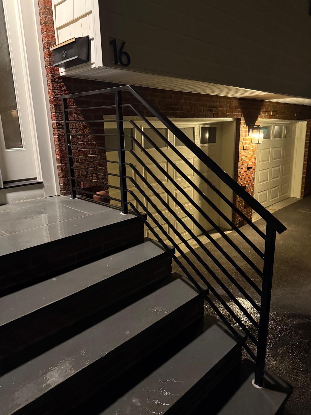 Exterior stairs and black railing leading to a brick townhouse entry marked 16 at night