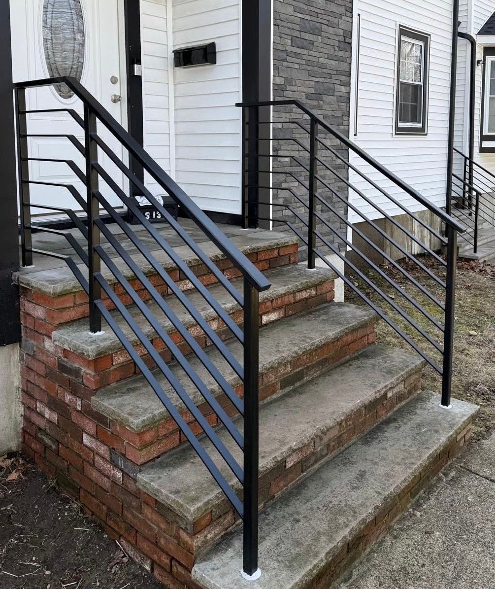 Brick porch steps with black metal handrails on both sides and a white house exterior