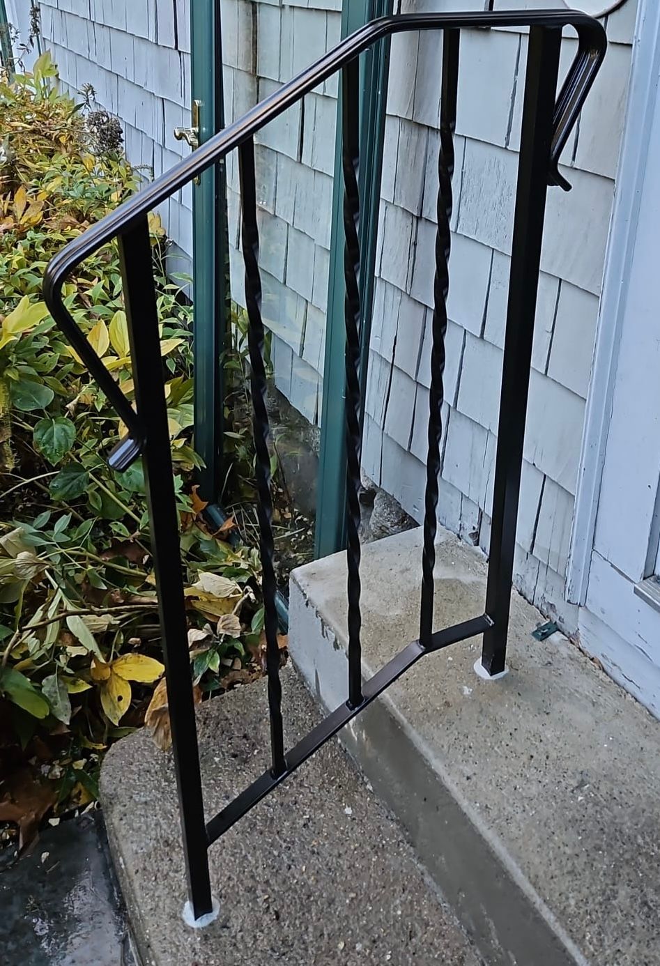 Black metal railing beside concrete steps at a blue house entrance, with a small garden on the left