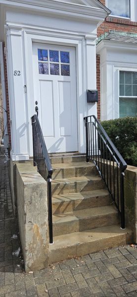 A white front door with a transom window, reached by concrete steps with black metal railings, labeled number 82.
