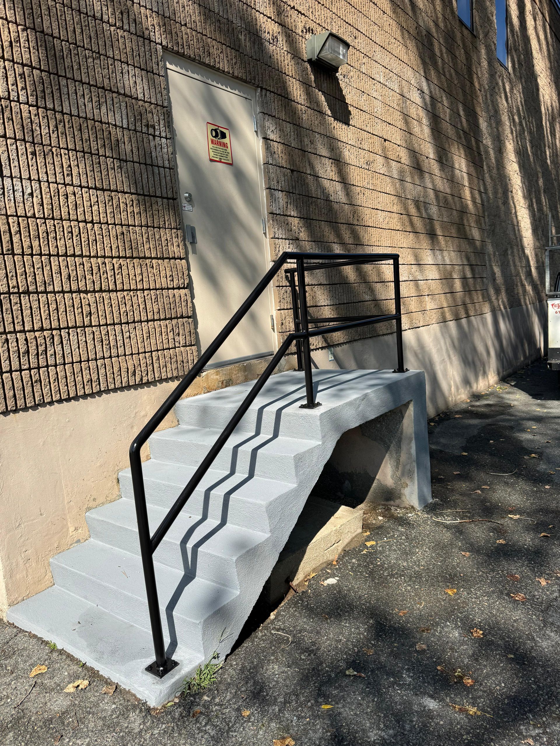 Accessible ramp and stairs with black railings beside a beige brick building and metal door