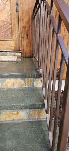Stone steps with a brown metal railing lead up to a wooden door with a rustic finish.