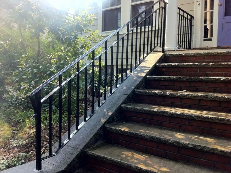 A set of brick stairs with stone treads and a black metal handrail leading to a house entrance.