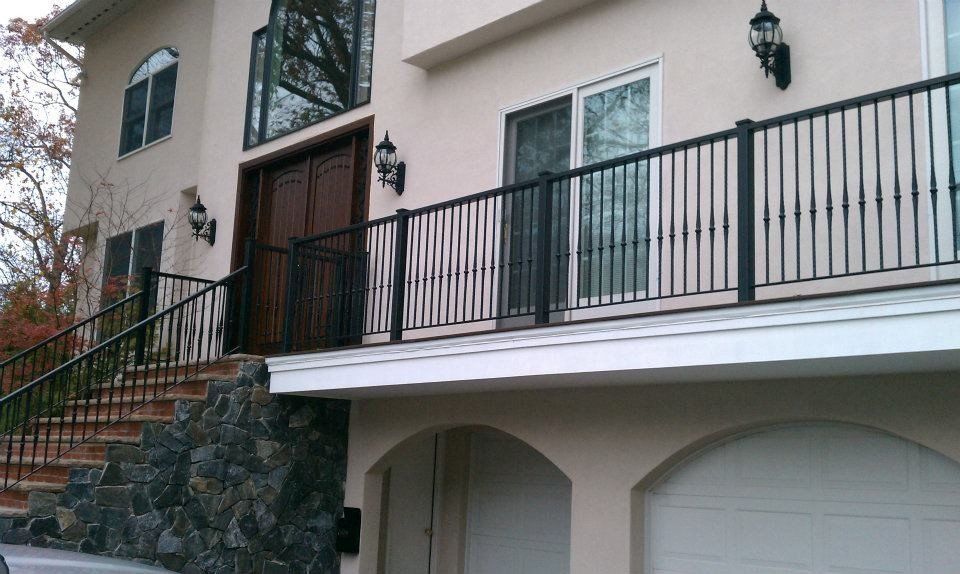 A two-story light-colored house with a dark stone foundation, a black metal railing, and a multi-car garage.