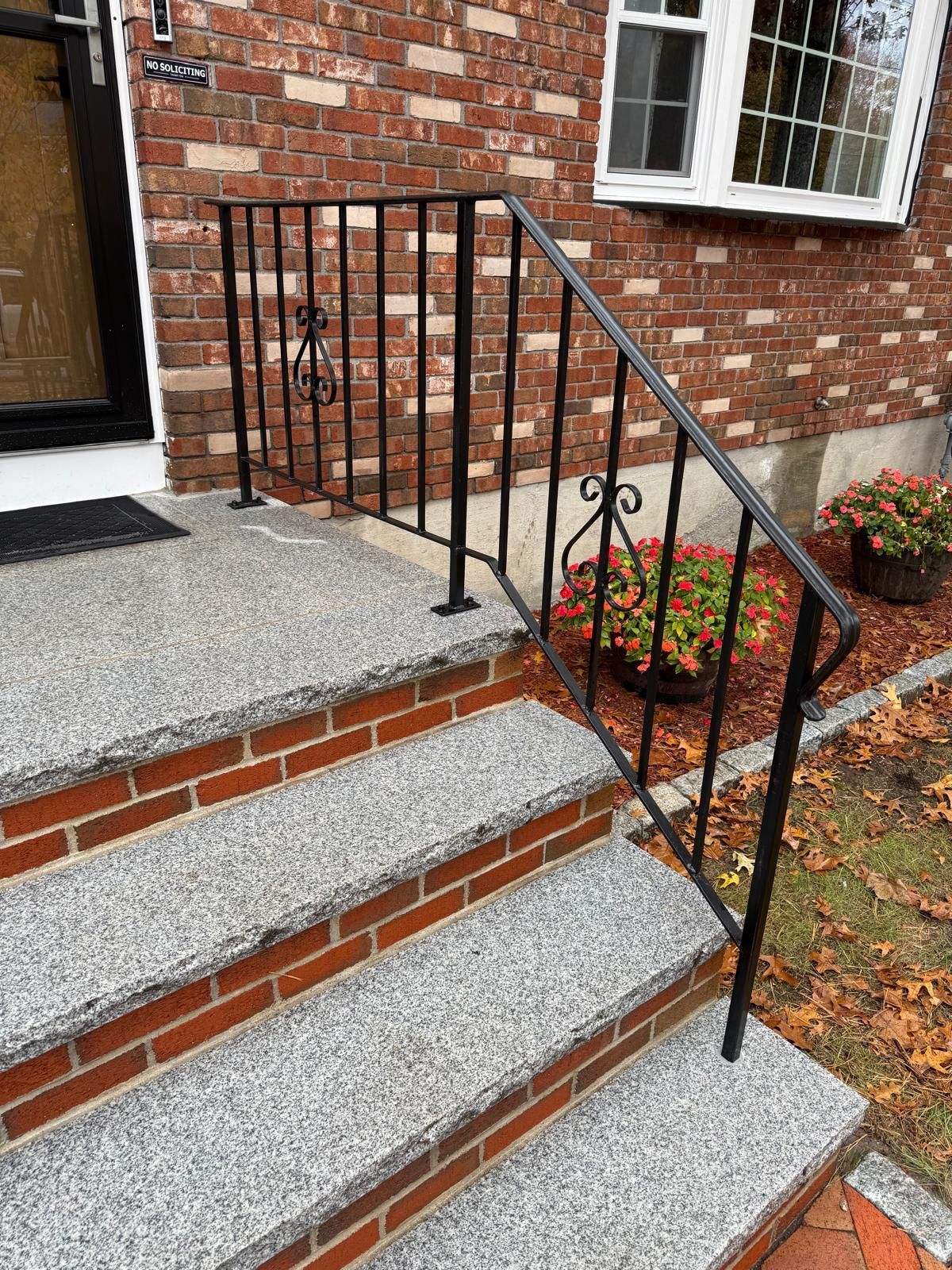 Front steps of a brick house with a black metal handrail and potted flowers beside the entrance