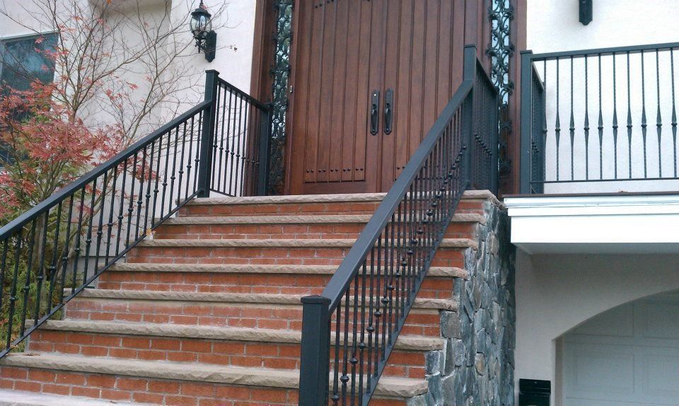 Brick staircase with black iron railings leading up to wooden double doors at the entrance of a house.