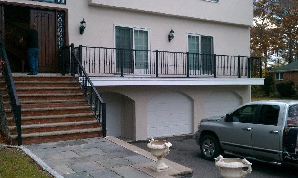 A beige house with stairs leading to a deck, two garage doors, and a pickup truck parked in the driveway.