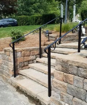 Stone outdoor steps with black handrails leading up a landscaped walkway