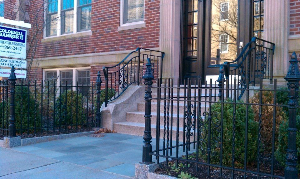 A brick building entrance with stone steps, a black iron fence, and a signage board on the left.