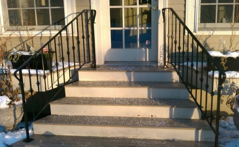 Front steps of a house with black railings, snow on the sides, and a glass front door