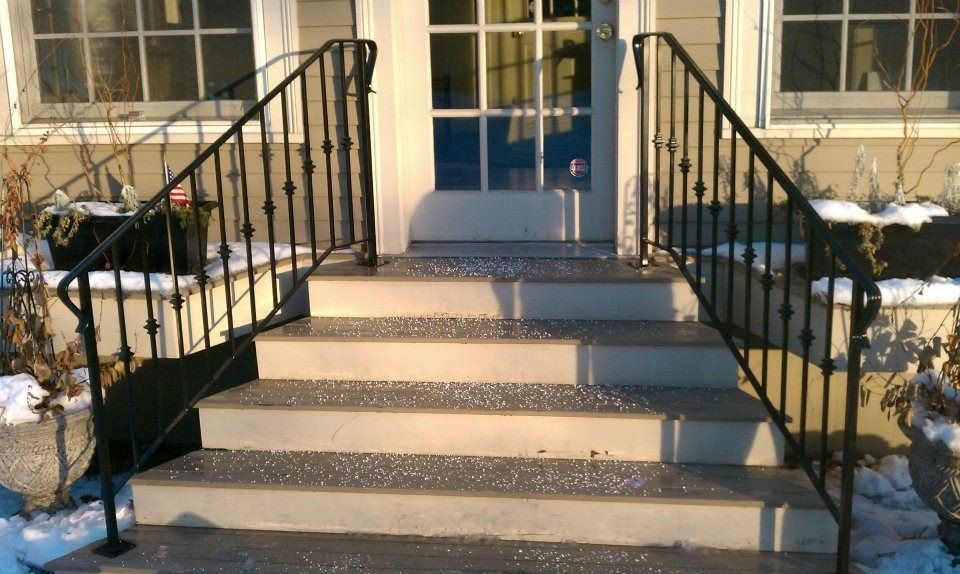 Concrete front steps with black metal railings leading to a house entrance covered in light snow.