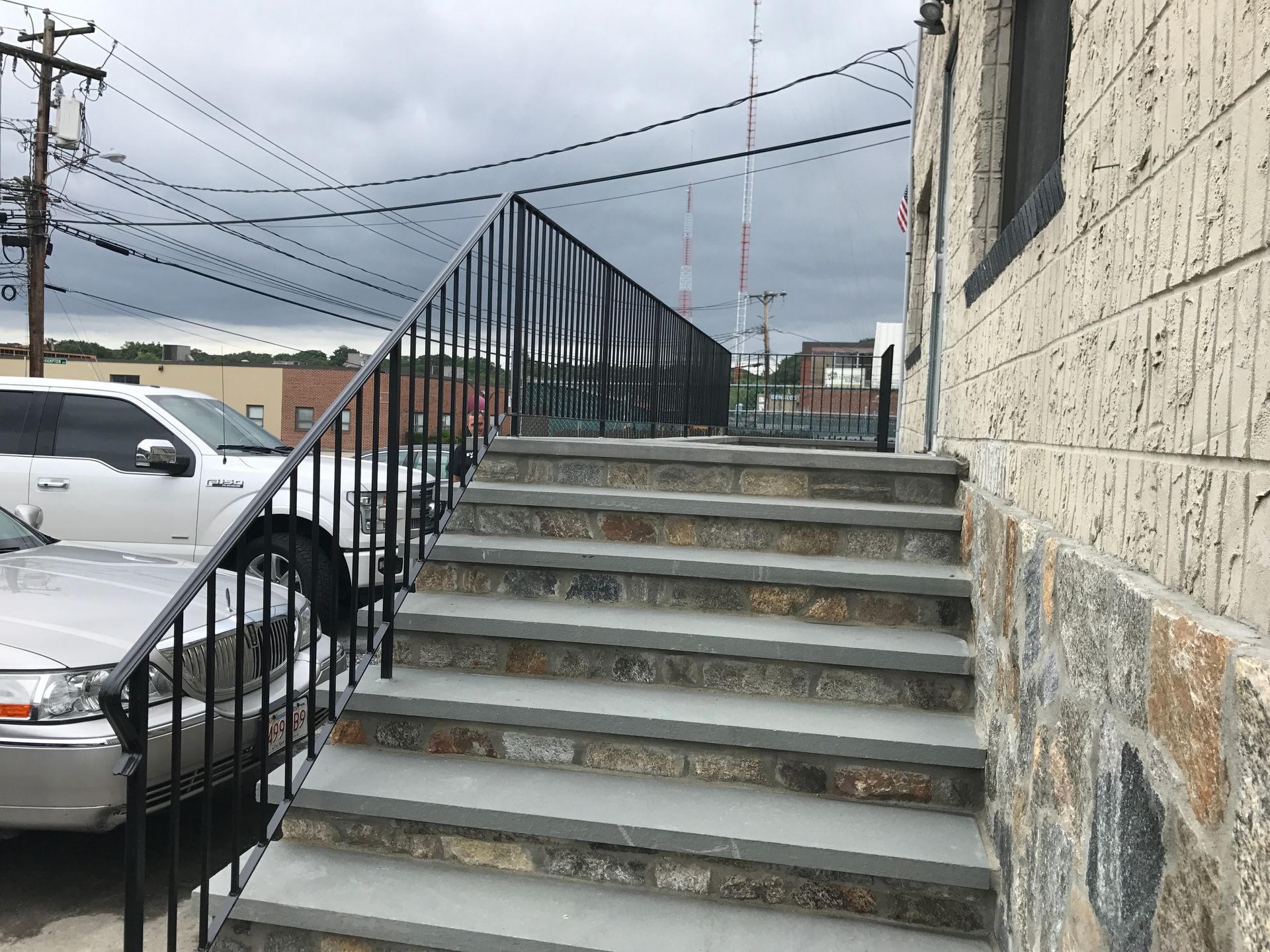 Outdoor concrete stairs beside parked cars and a stone building under power lines