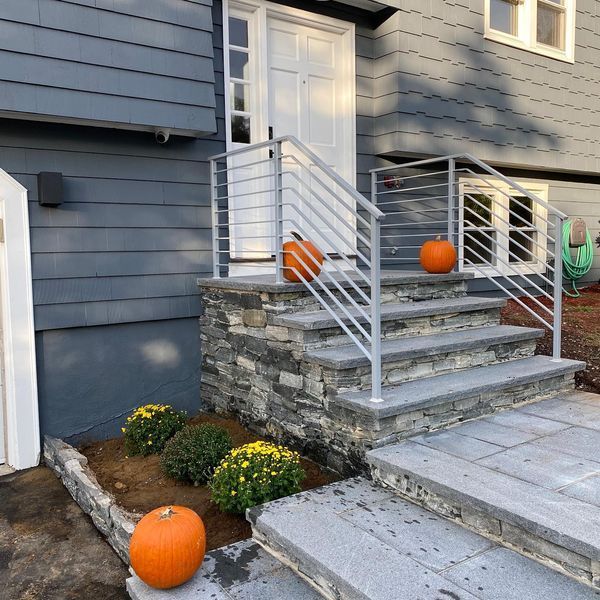 Gray front steps with stone veneer, horizontal metal railings, and orange pumpkins placed for fall decor.