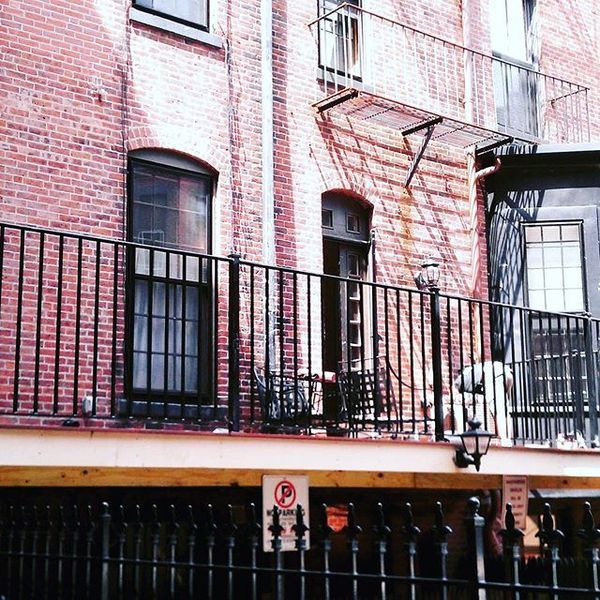 A brick building exterior with a raised wooden deck, black metal railings, a doorway, and windows.
