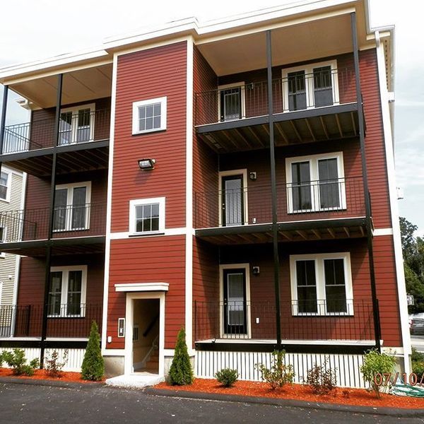 A red, three-story apartment building with balconies and white trim, viewed from the street level.