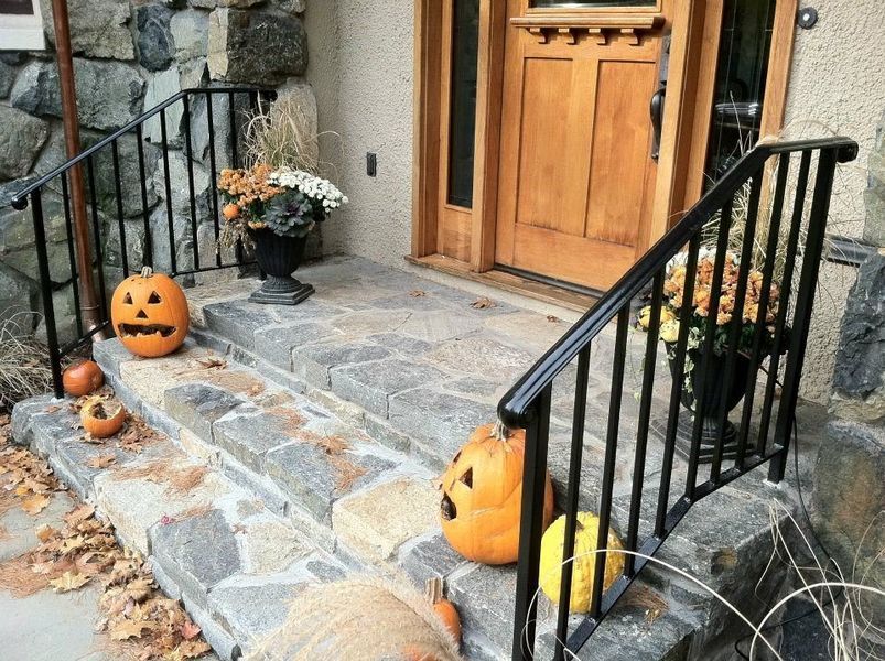 Stone steps leading to a wooden door decorated with pumpkins and potted plants for the fall season.
