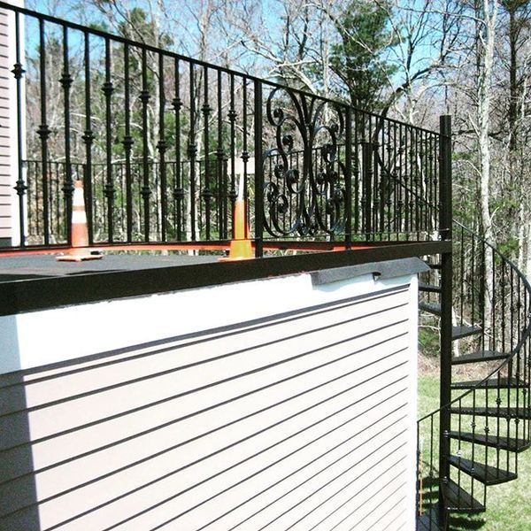 Black iron deck railing with decorative scrollwork and a spiral staircase attached to the side of a light-sided house.