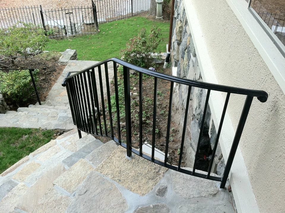 Black metal handrail beside stone outdoor steps next to a house and garden path