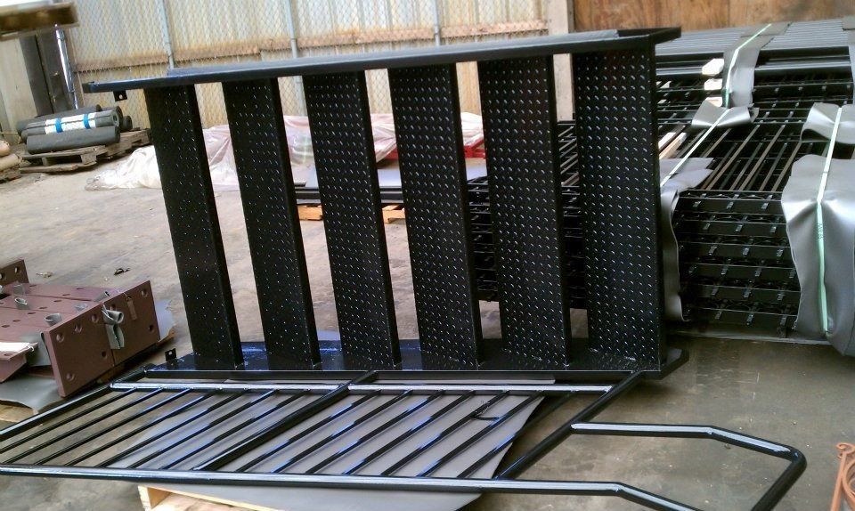 A stack of black, perforated metal stair treads and railings in a warehouse setting.