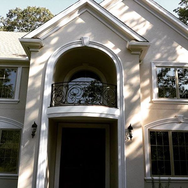 Two-story cream-colored house with a central arched entrance, wrought iron balcony, and symmetrical windows.