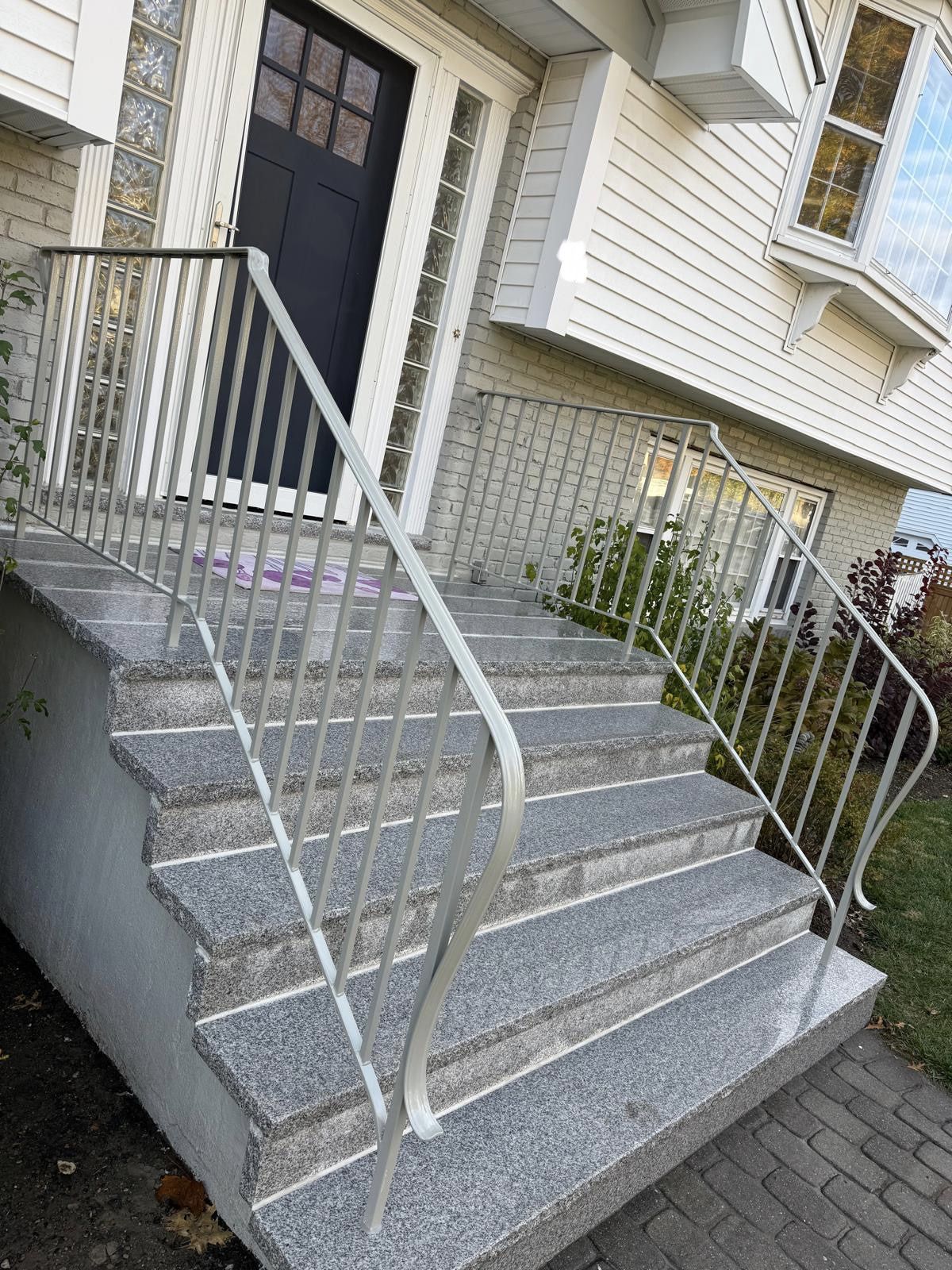 Front steps with gray stone stairs, white railings, and a dark front door on a house exterior
