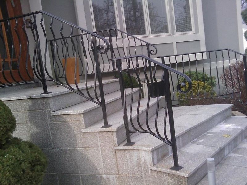 Wrought iron railing with decorative curved balusters installed on stone steps leading up to a house entrance.