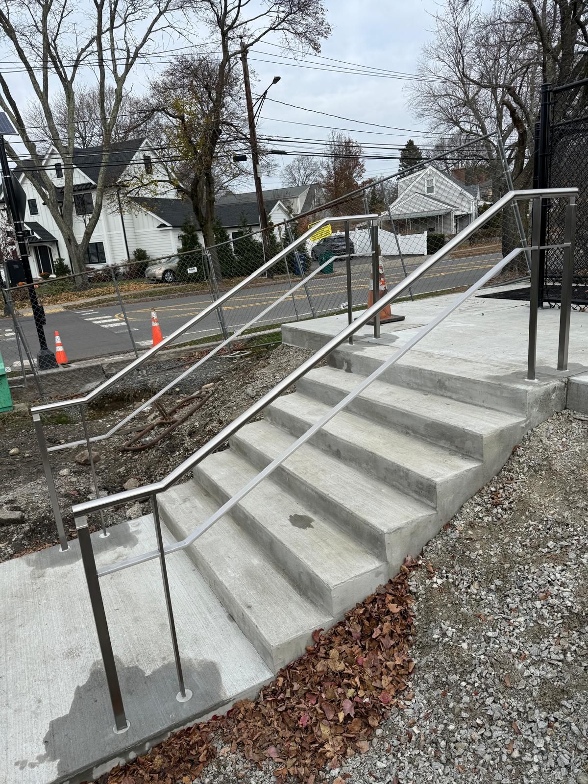 Concrete outdoor stairs with metal railing descending a sloped walkway beside a residential street