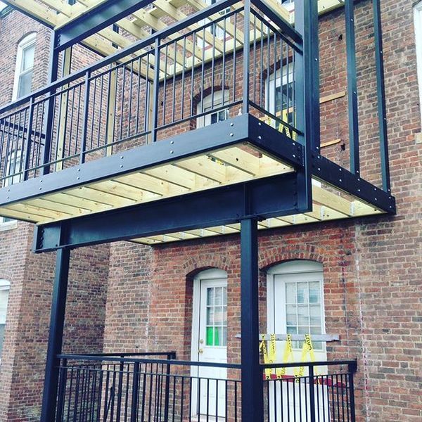 A newly constructed black steel balcony with a wooden deck and railing attached to a historic red brick building.