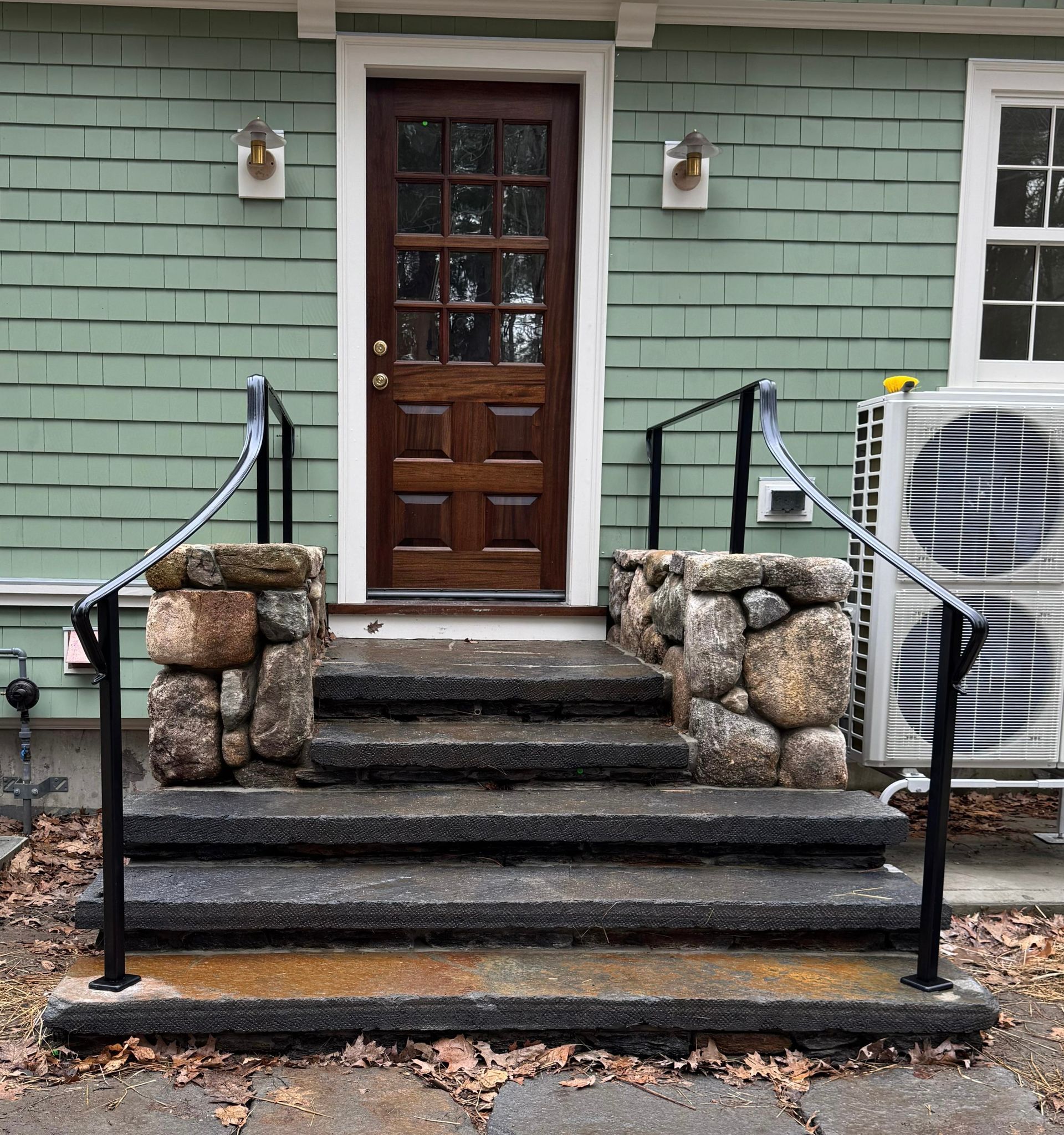 Front porch with dark wood door, stone steps, black railings, and mint green siding