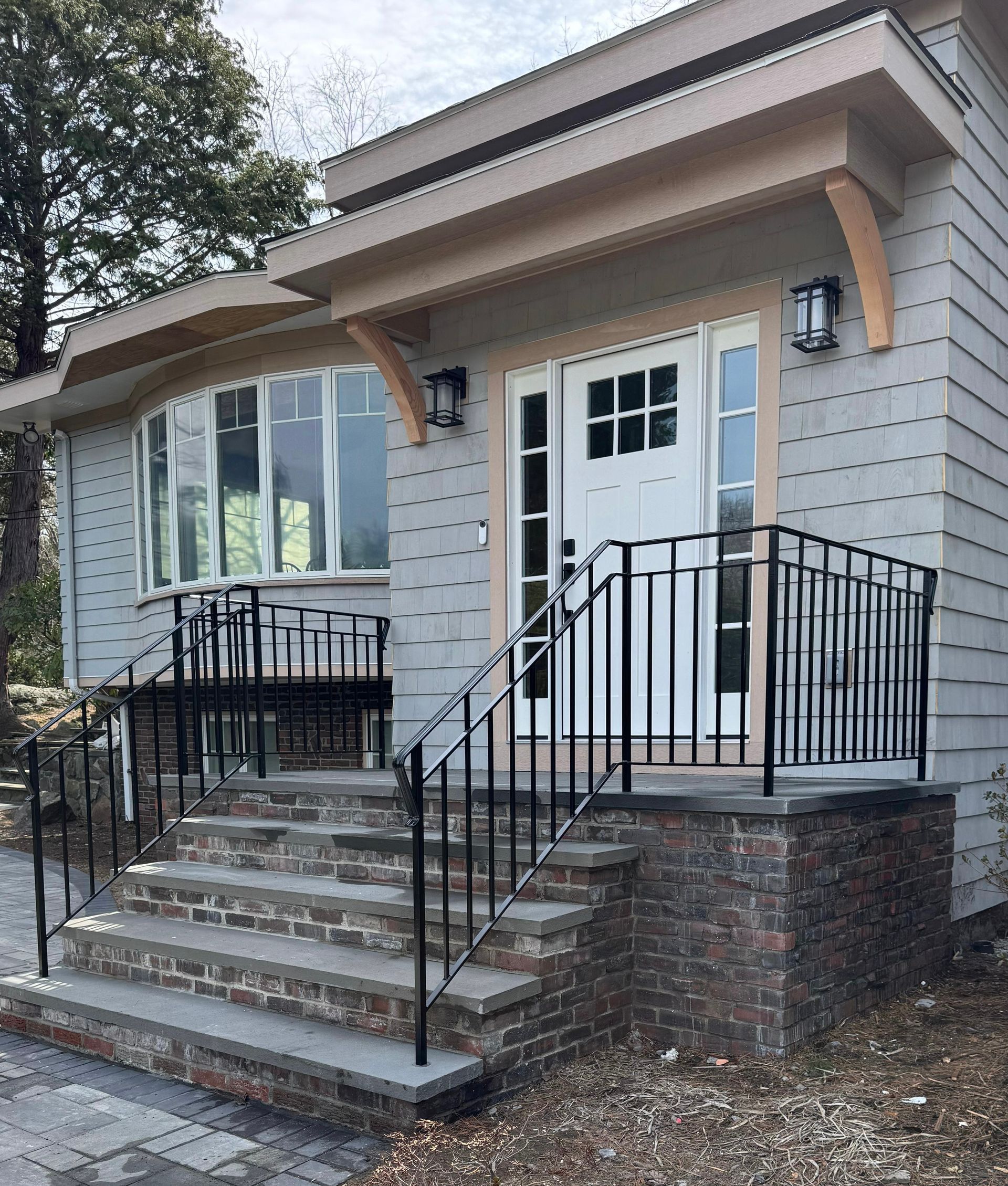 Front entrance of a small gray house with steps, black railings, and a white door