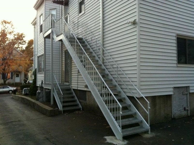 A side view of a white multi-story house with an external metal staircase leading up to a second-floor entrance.