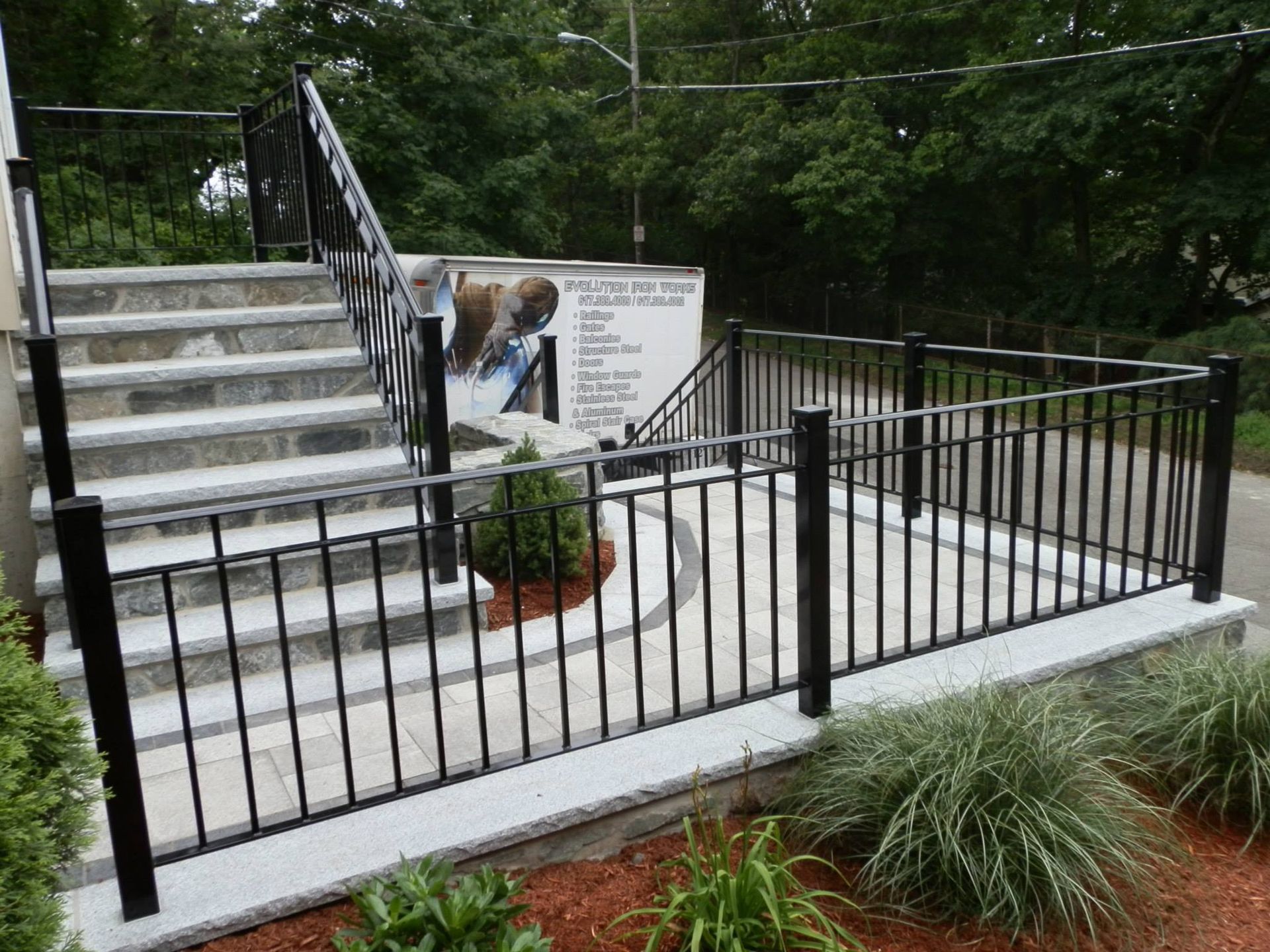 Black metal fence around a stone stairway and ramp in a landscaped outdoor area