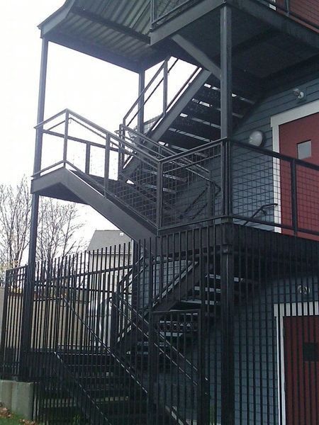 Exterior metal fire escape stairs with railings, attached to the side of a blue building with a red door.
