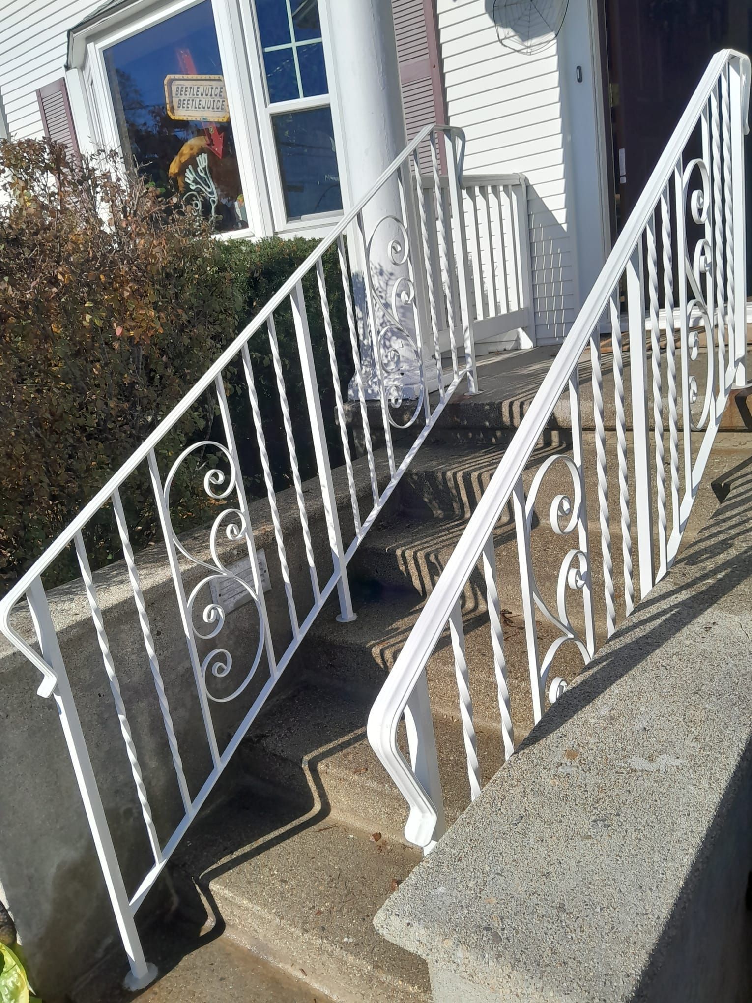 White front steps with decorative railings leading to a house entrance beside a bush and blue-trimmed windows