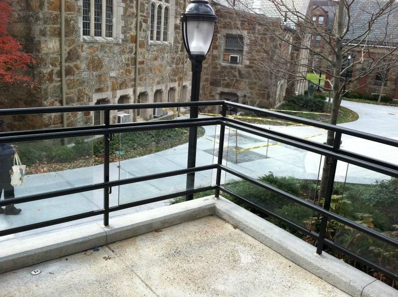 A stone building viewed from a concrete balcony with black metal railings and a vintage-style street lamp.