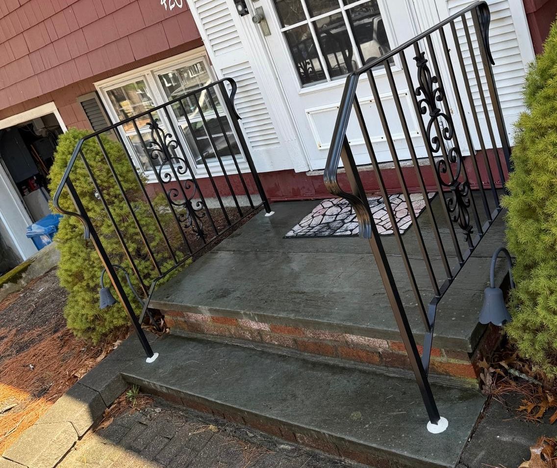 Front porch with black railings, concrete steps, and a white door on a red house.