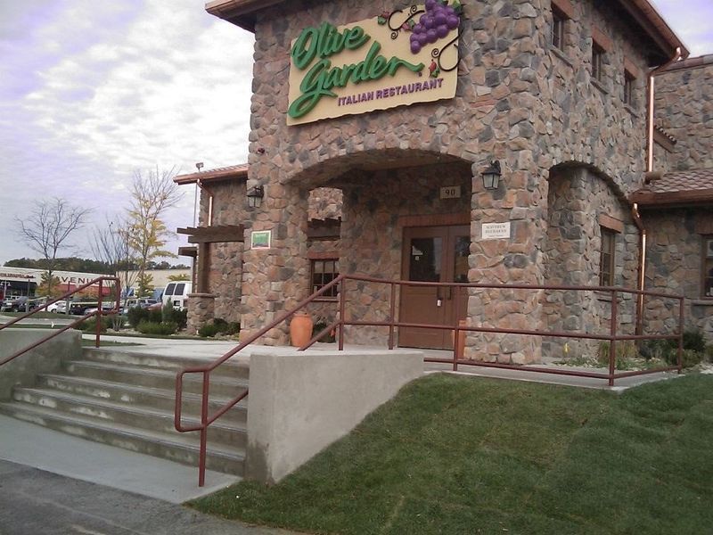 Stone-faced Olive Garden restaurant exterior with concrete stairs and a metal railing leading to the front entrance.