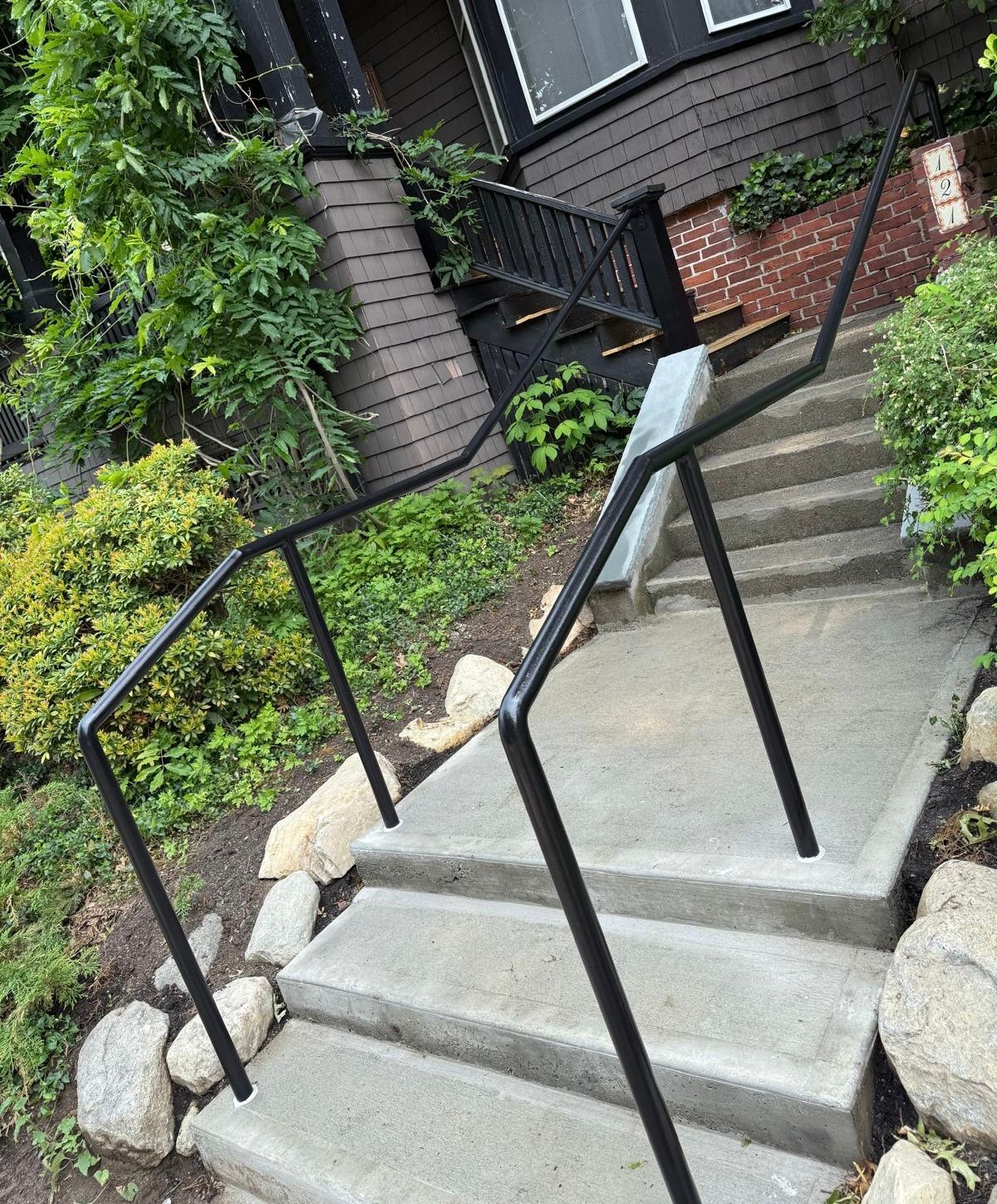 Steep concrete steps with black handrails leading to a house entrance surrounded by greenery