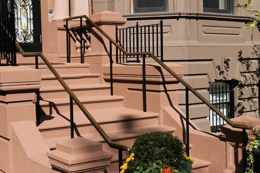 Tan stone steps lead up to a building entrance with dark metal handrails and a small potted plant in the foreground.