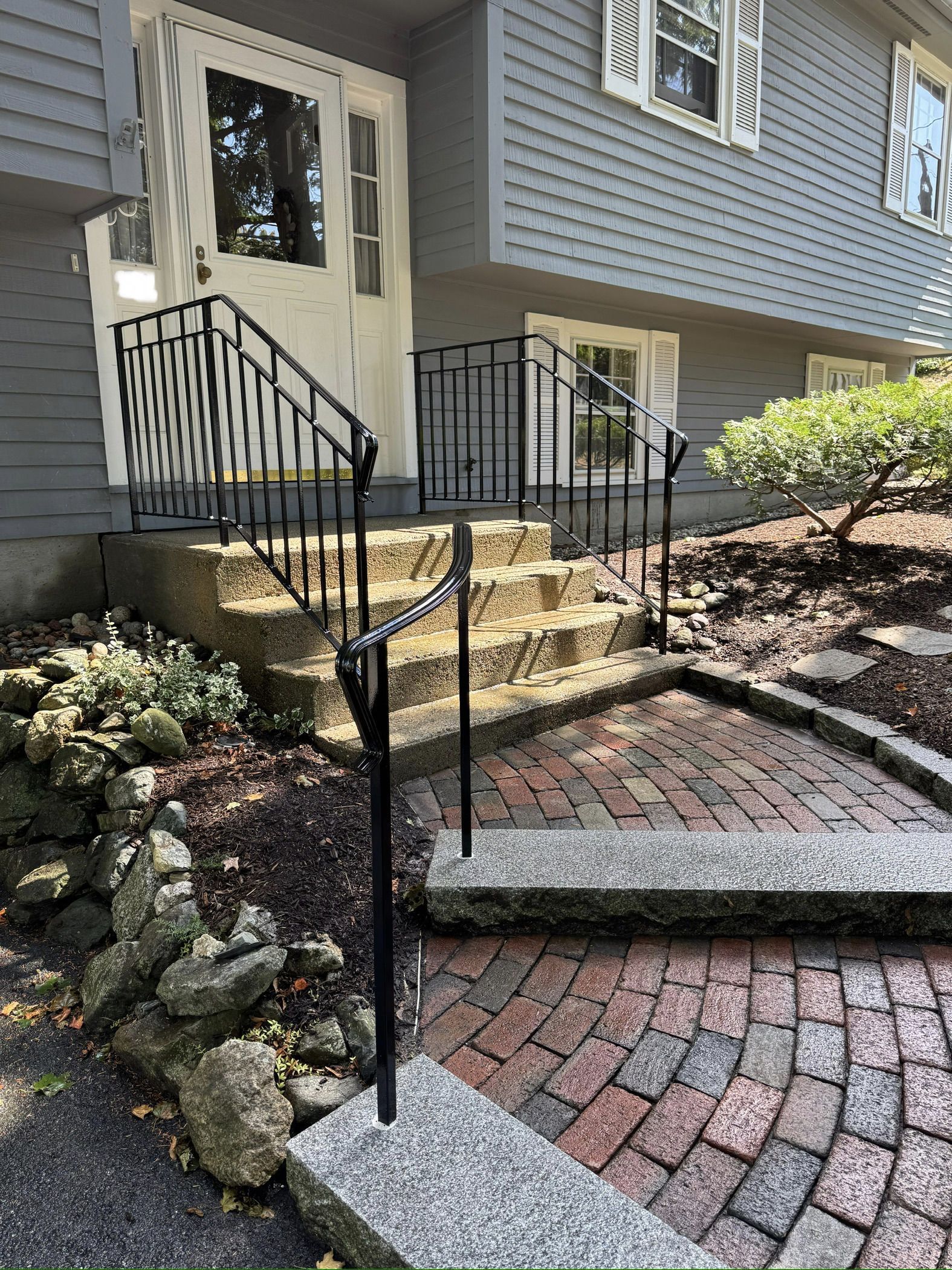 Front steps and walkway with black railings leading to a house entry and side garden steps