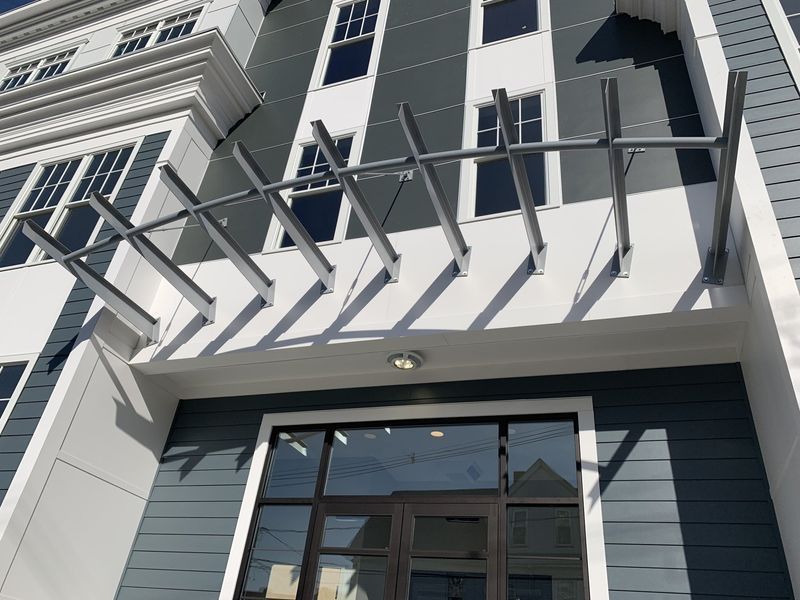 Building entrance featuring a modern grey metal canopy over a glass door, set against a dark blue and white facade.