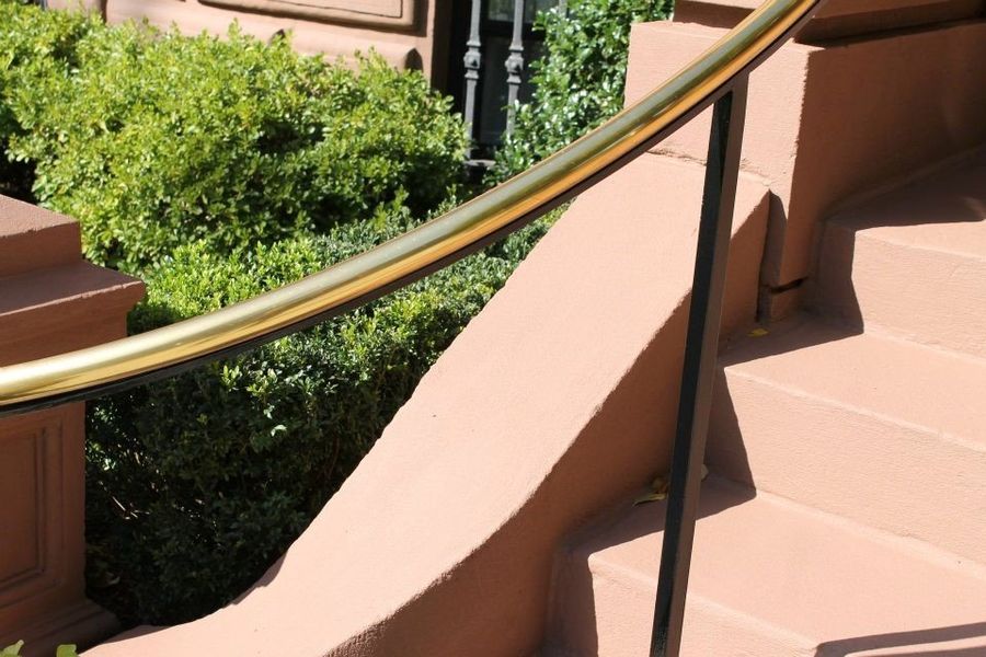 A metal handrail runs along beige stone steps next to a green bush.